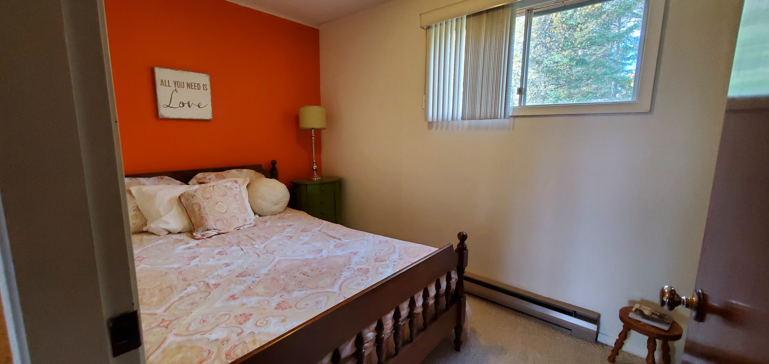 A small bedroom with a big bed, a window, and an orange accent wall.