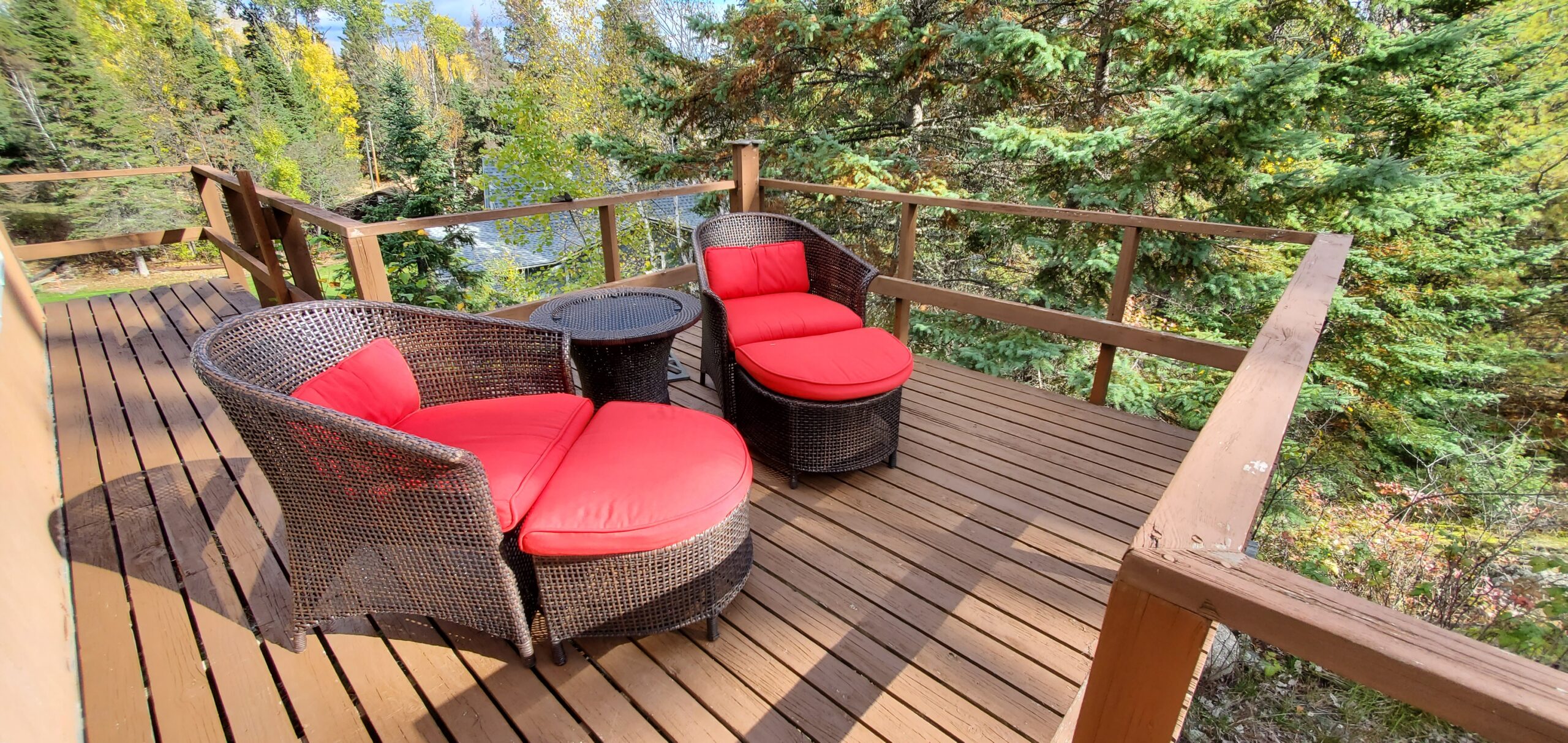 A big deck with two cushioned patio chairs, looking out over trees.