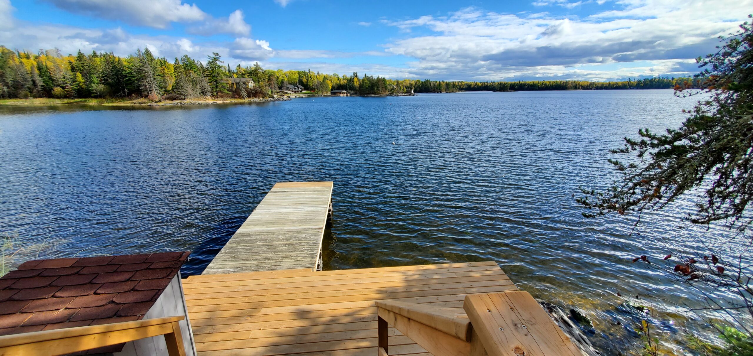A wooden dock extends out from a big deck into a blue lake.