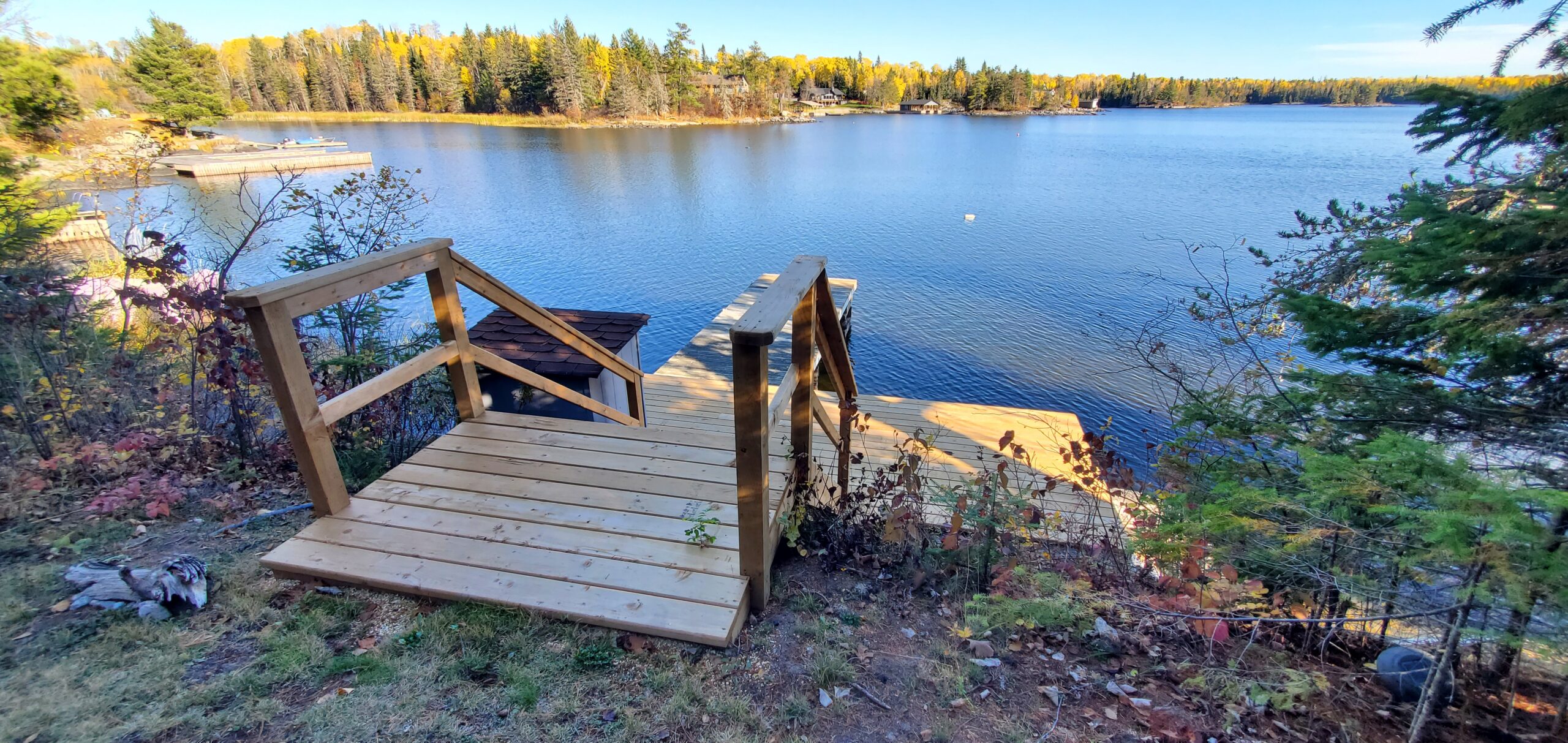 Wooden stairs lead down to a dock, which extends out into a blue lake from a big deck.