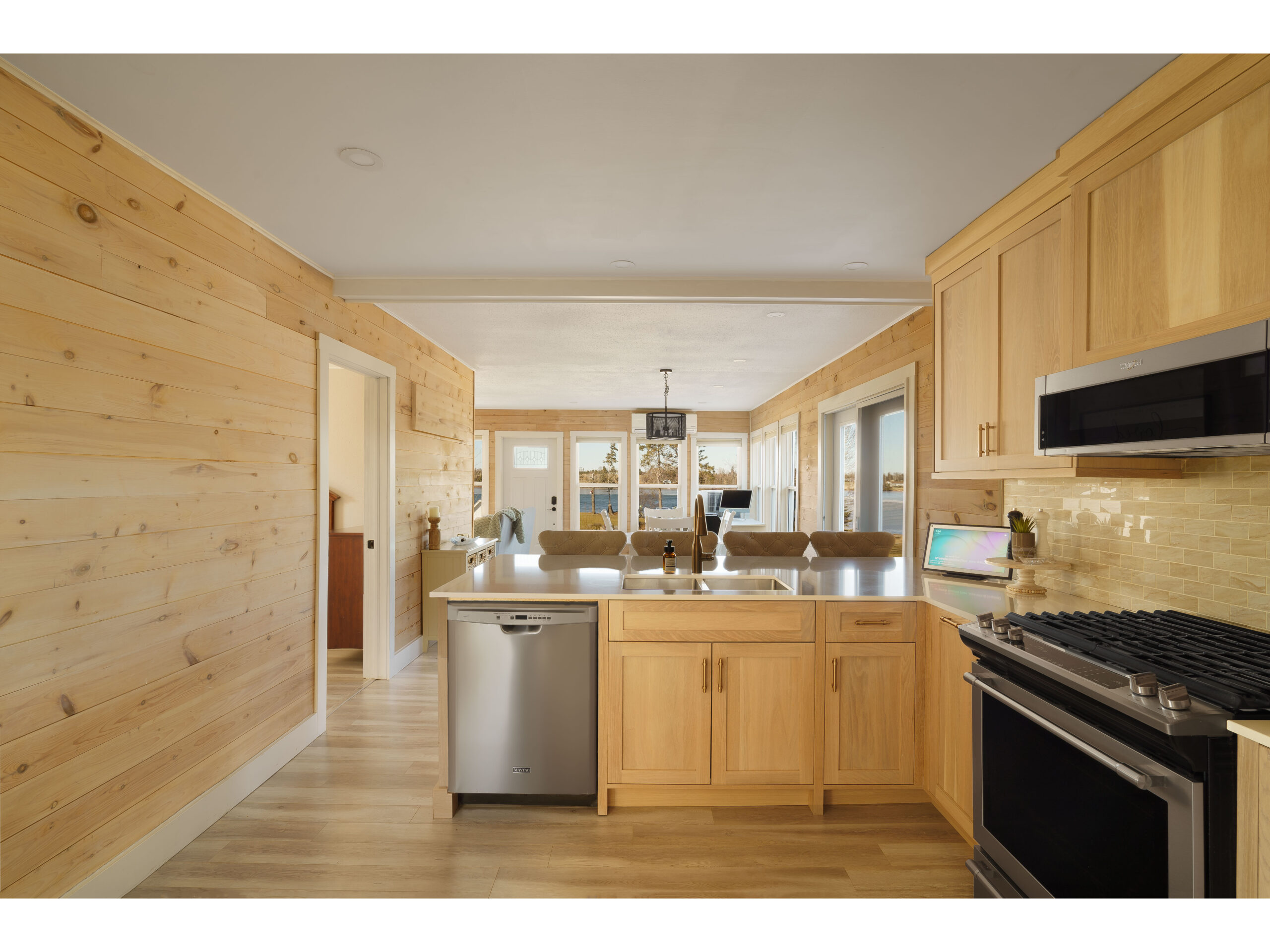 A small but open kitchen with a large peninsula and barstools, wooden cabinets that match the wood-panelled wall, and stainless steel appliances.