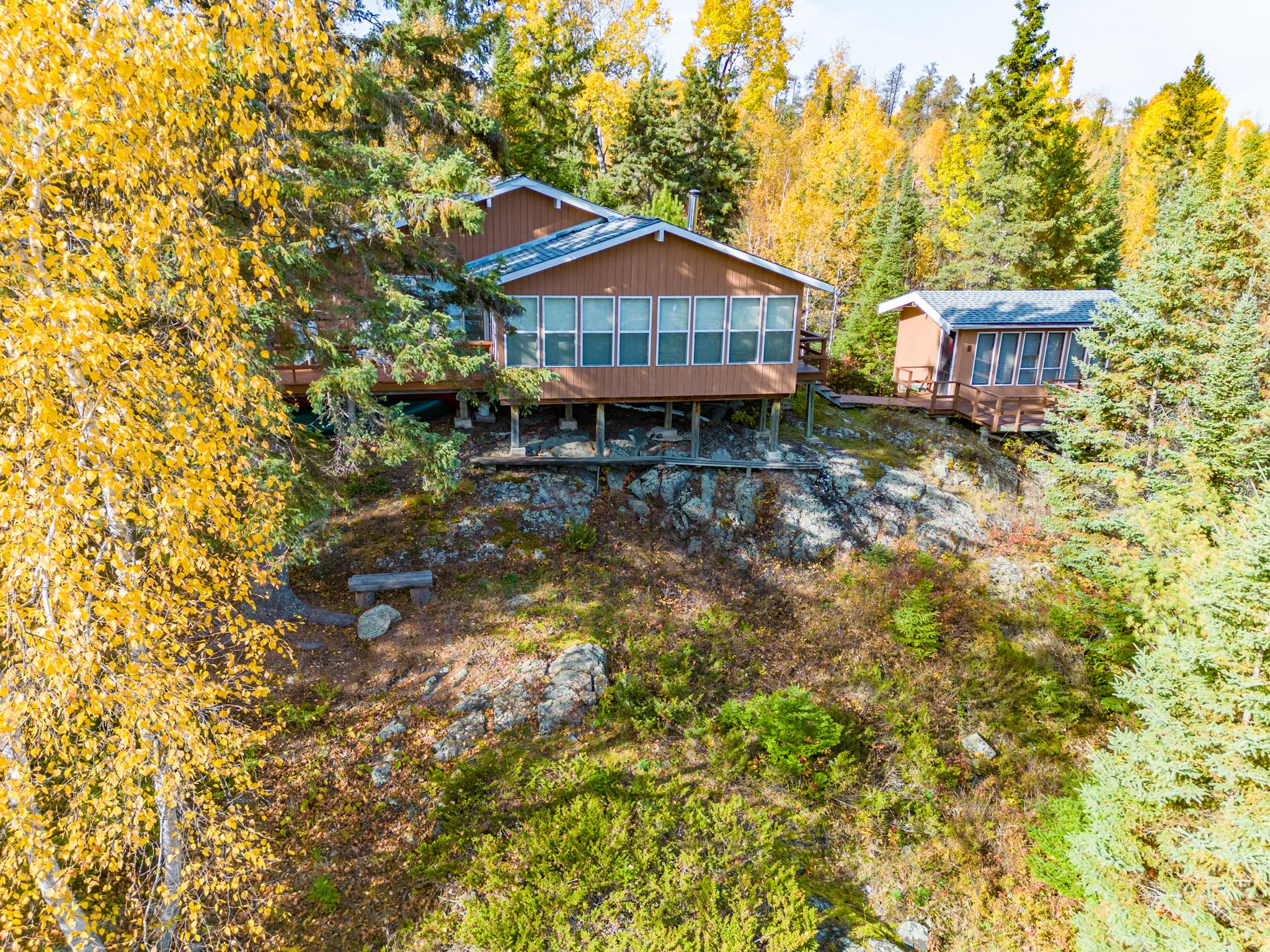 A lakefront cottage with lots of windows sits on a high slope, surrounded by trees.
