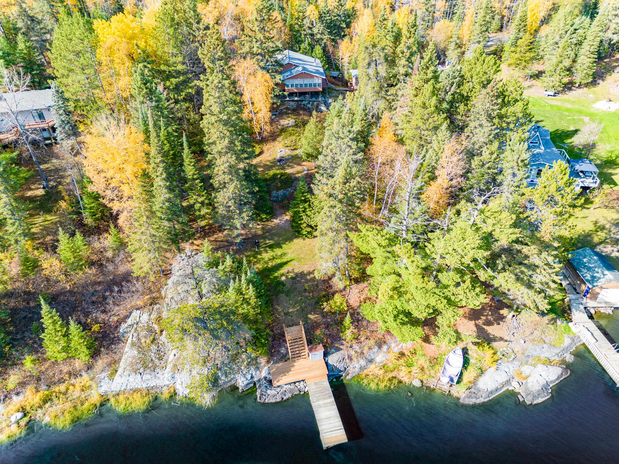 Overhead view of a lakefront property surrounded by trees, with a dock extending into the water.