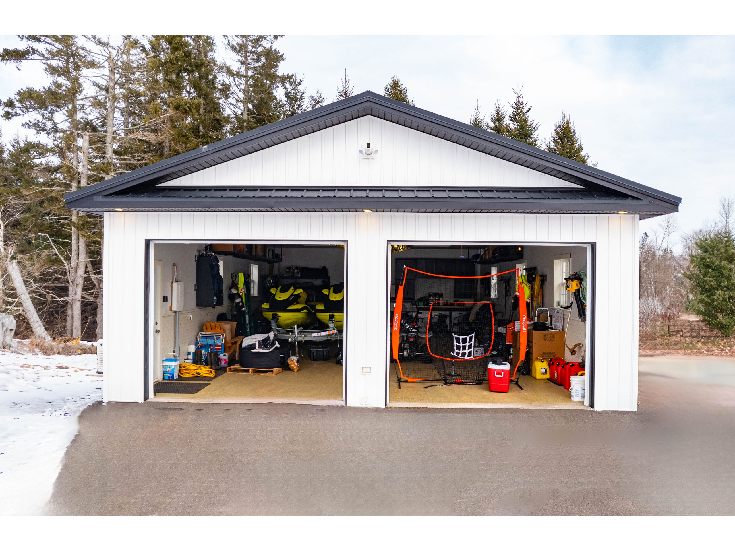 A detached double garage with a white exterior and black trim. Both doors are open, revealing lots of storage space.