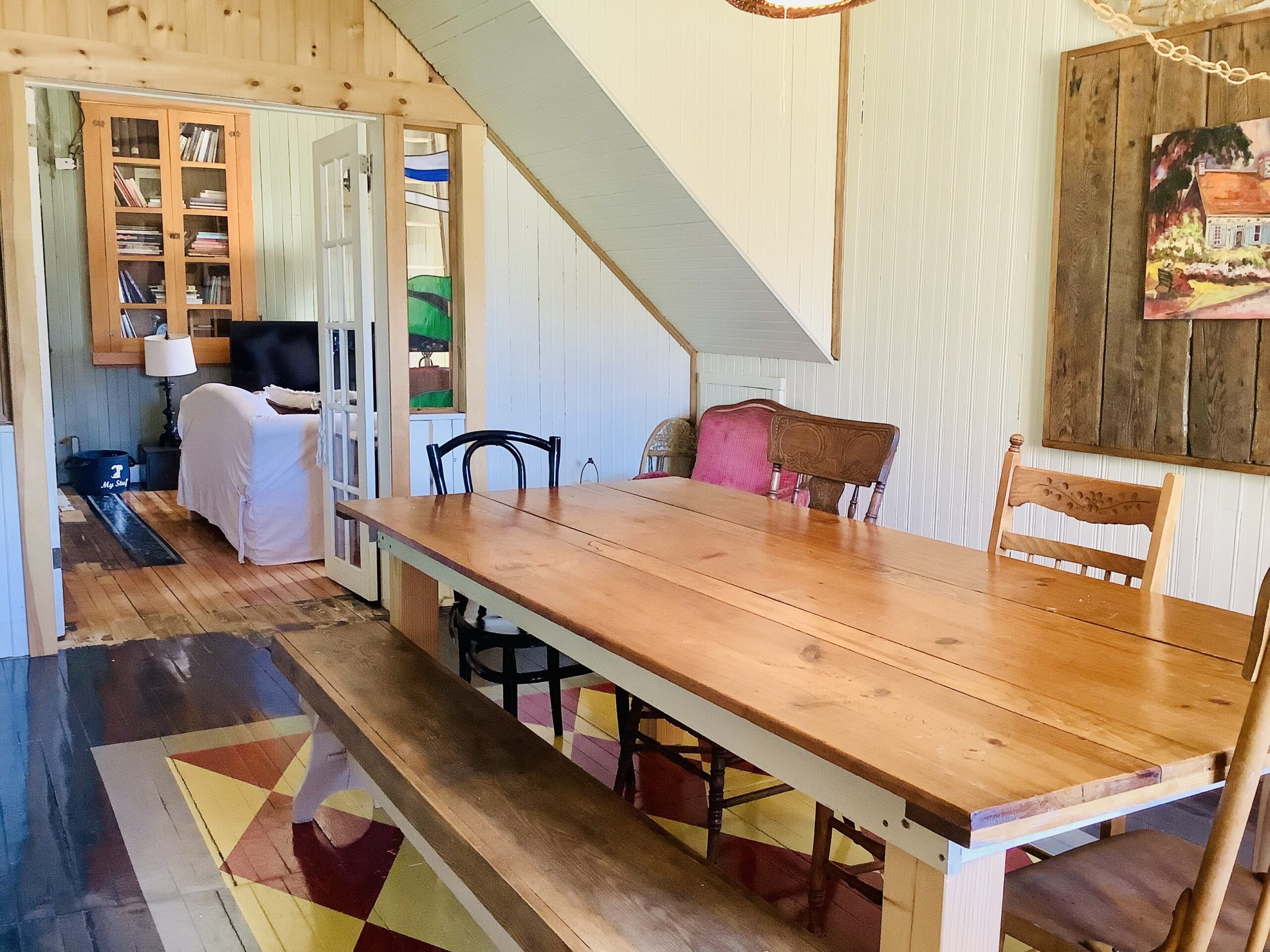 A dining area with a farmhouse-style table that has a bench on one side and mismatched wooden chairs around the other side. The walls are white-painted wood.