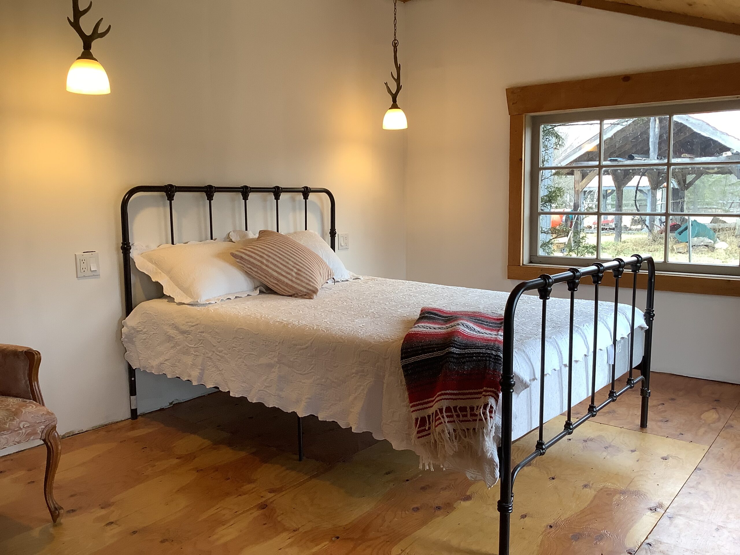 A bed with a black metal frame. Two light fixtures with a minimal antler design hang down over the bed, and there is a big window on the exterior wall.