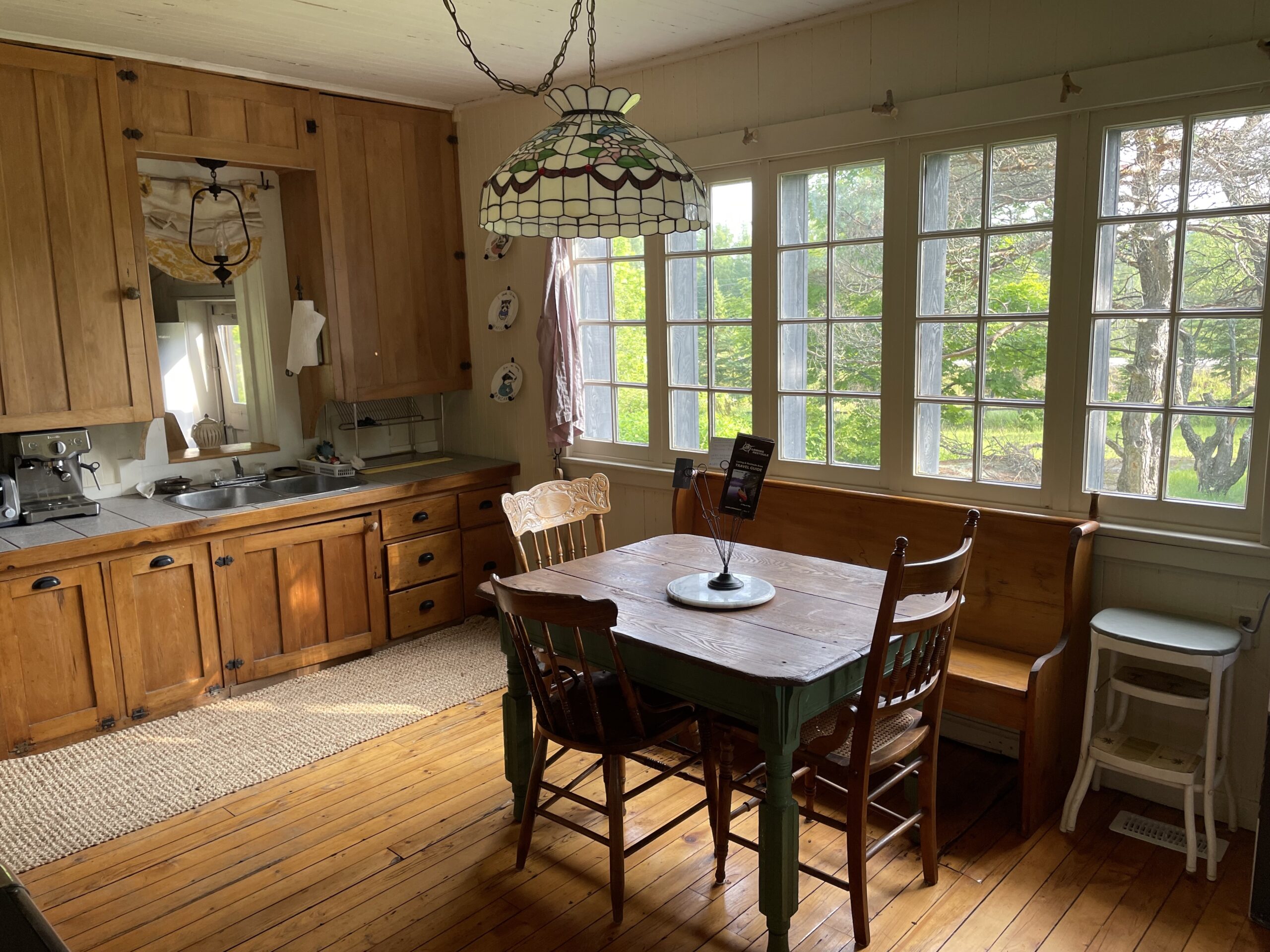 A kitchen with a small table and chairs, hardwood floors, wooden cabinets, and big windows across the exterior wall.