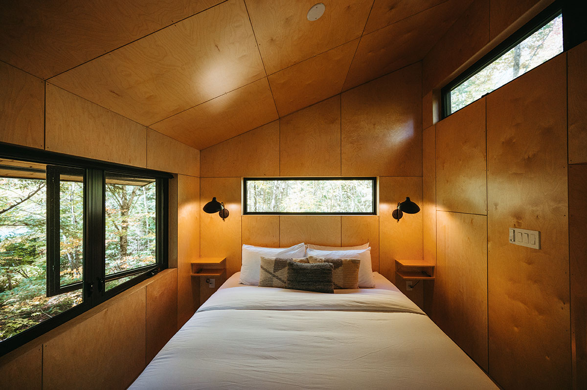 A bed with a white bedspread takes up most of the treehouse's attic, which is surrounded by large windows.
