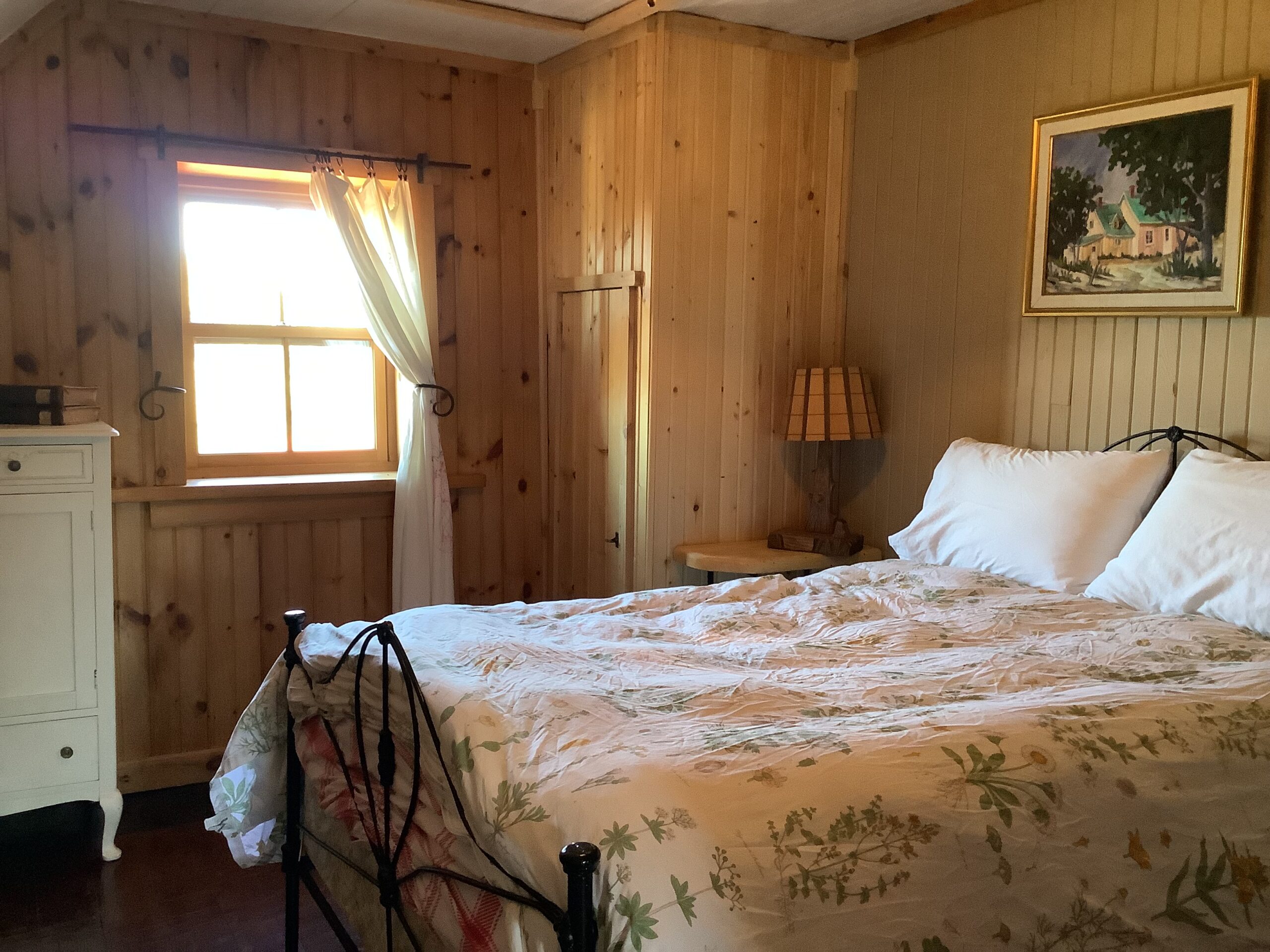 A small bedroom with a window, wood-panelled walls, and a bed with a floral bedspread.