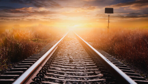 The sun's rays hitting a train track that cuts through grassland